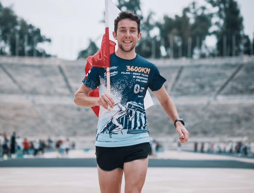 Mężczyzna w odzieży sportowej biegnie z flagą kraju